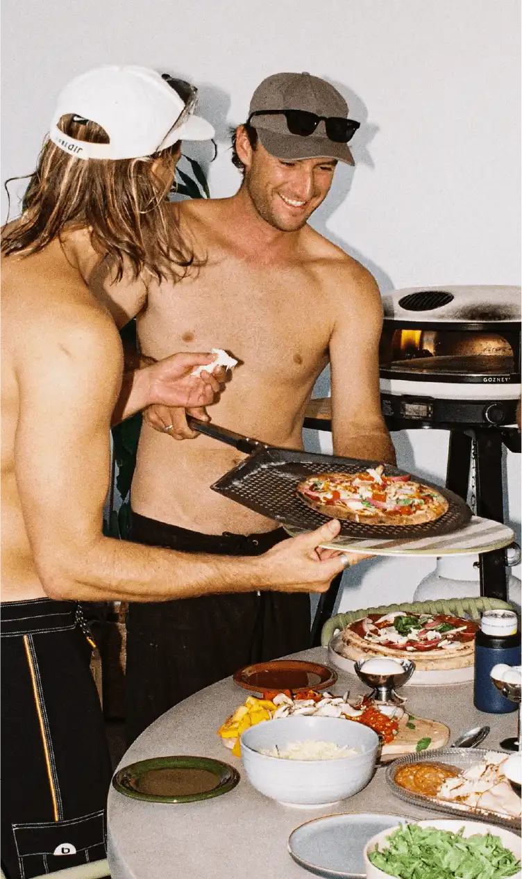 Two people serving a freshly cooked pizza off a Gozney peel